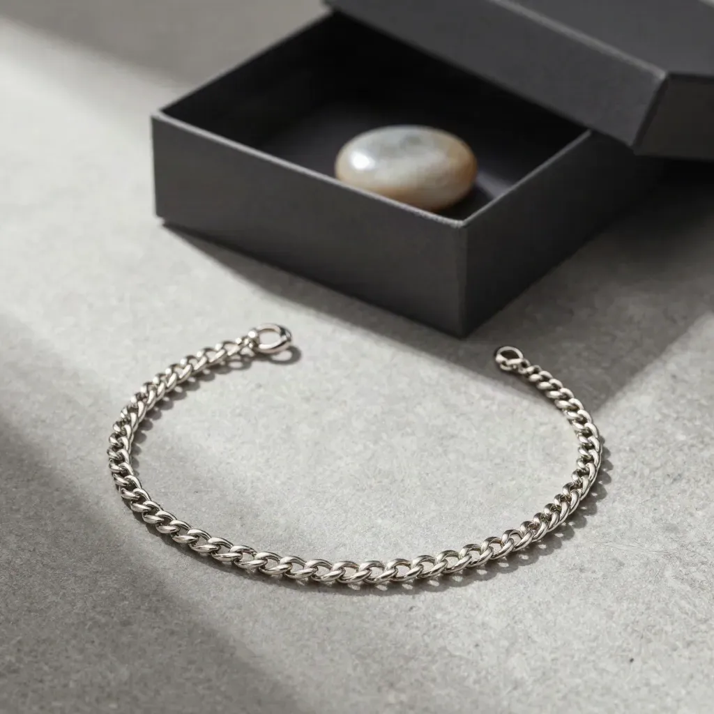 Cadena de plata 925 sobre tela gris piedra con caja abierta y piedra pulida.